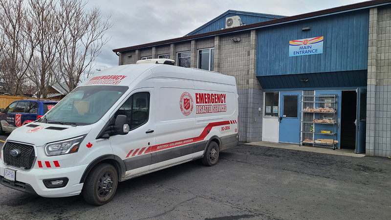 The Salvation Army Emergency Disaster Services van parked outside a Salvation Army community building, with the building entrance and signage visible behind it.