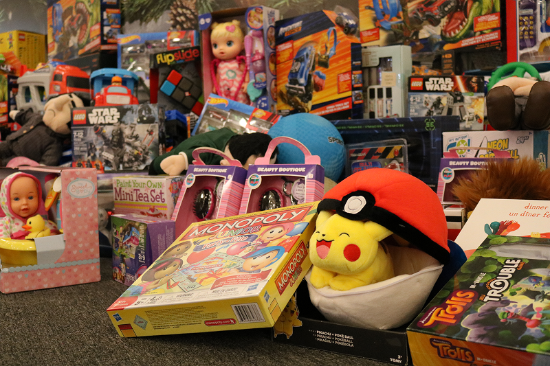 A large assortment of donated toys and games arranged on the floor, including board games, dolls, stuffed animals, puzzles, and boxed toy sets in colorful packaging.