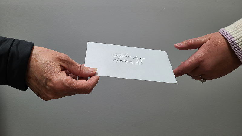Two pairs of hands reaching toward each other as one person hands an envelope to another against a neutral background.