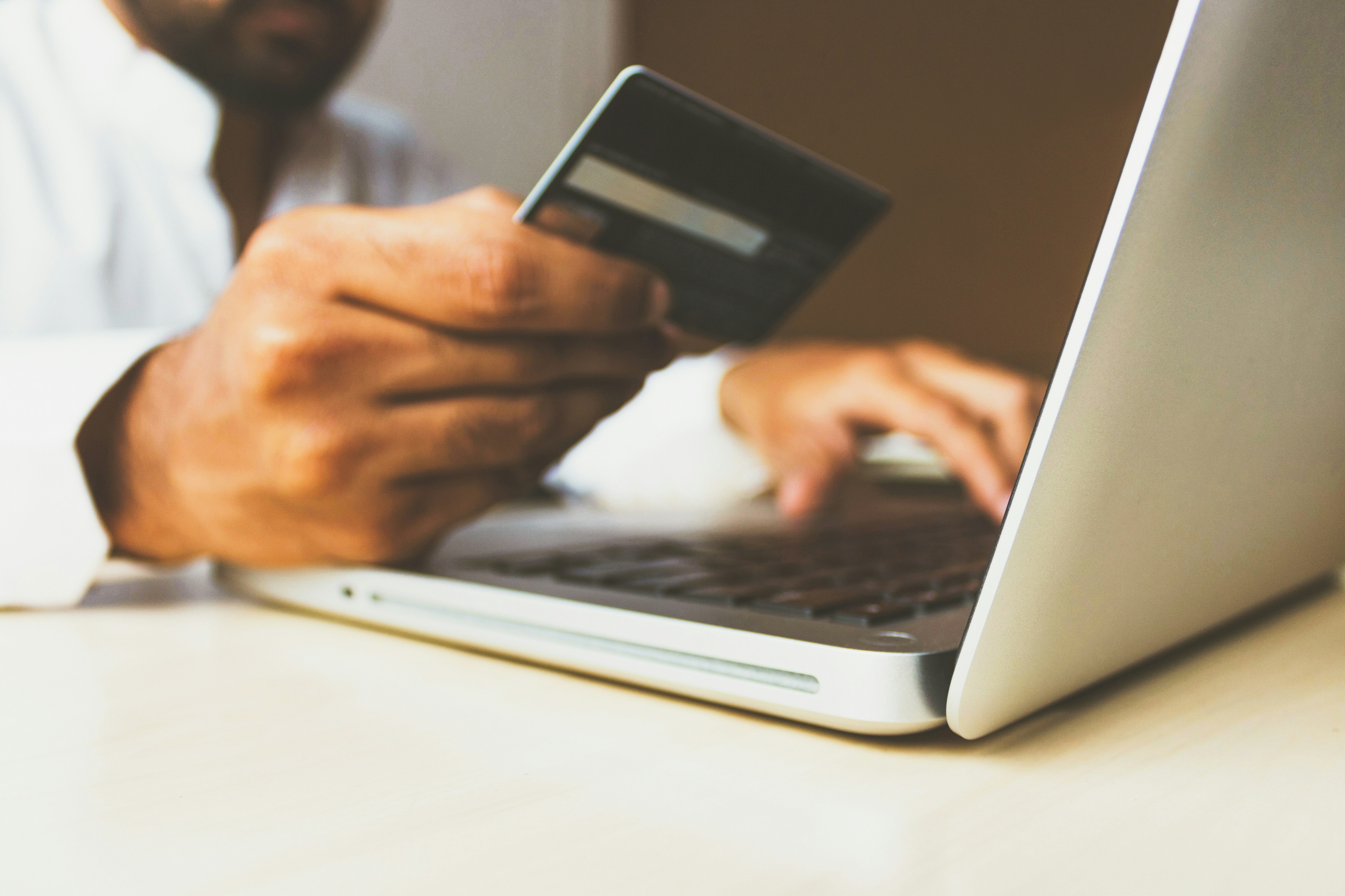 A close-up view of hands holding a credit card while using a laptop on a desk, suggesting an online payment or donation being made.