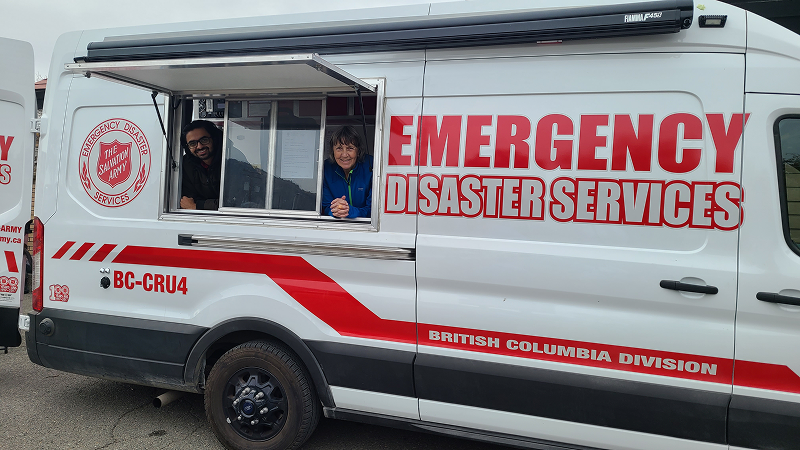 The Salvation Army Emergency Disaster Services van parked outdoors with its side service window open, showing people inside the vehicle and large red signage reading Emergency Disaster Services on the side.